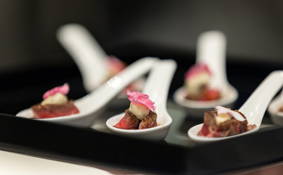 The waiter holds a Set of festive appetizer canapes on bread on a black tray as an event dish. Buffet table. Catering. Delicacy. Haute cuisine. 