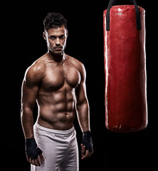 Fototapeta na wymiar The warrior is always ready for battle. Studio shot of kick boxer working out with a punching bag against a black background.