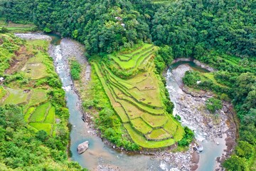 Bird's eye drone shot over the rice terraces of Banaue in the Philippines, surrounded by trees and bushes and a river.