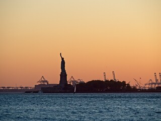 The sun sets over New York City with the Statue of Liberty sitting atop Liberty Island in the New...