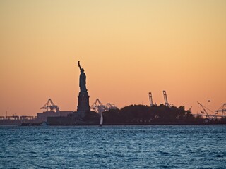 The sun sets over New York City with the Statue of Liberty sitting atop Liberty Island in the New...