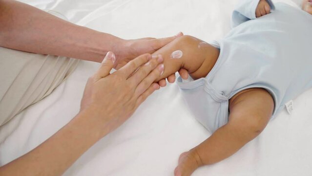 mother applying moisturizing cream on leg of her newborn baby