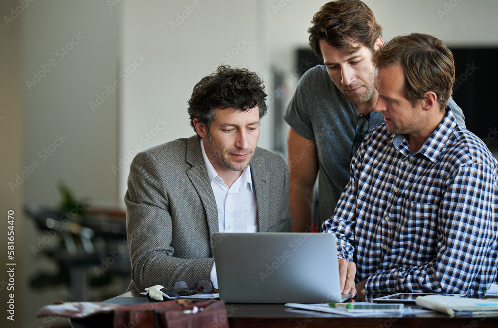 Poster adding some final touches to their project. three male coworkers working on a laptop together.