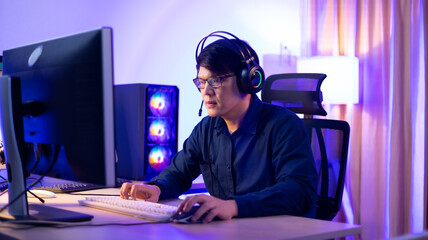 Fototapeta na wymiar Professional Asian male gamer playing video games on personal pc computer. Colorful neon light room. Esport online game.