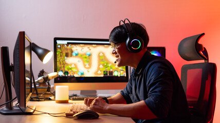 Professional Asian male gamer playing video games on personal pc computer. Colorful neon light...