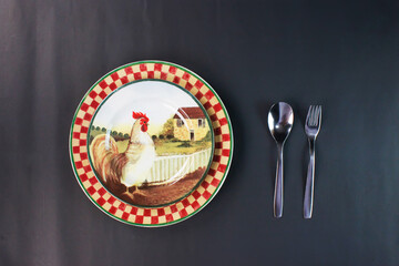 Chicken ceramic plate and a spoon, fork next to it. isolated on black background