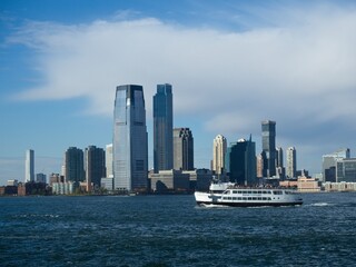 Fototapeta premium Looking back on Manhattan from the Hudson River and Liberty Island, as the towering high rises of Lower Manhattan loom above the river