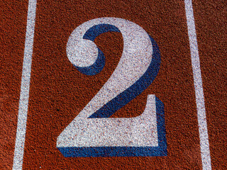 Close up lane number 2 on a new red running track with white lane lines and other markings.	