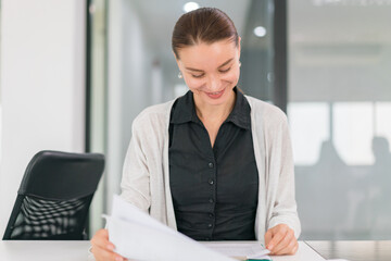 Focused on success and growth , Pretty young business woman working with computer while consulting some invoices and documents.