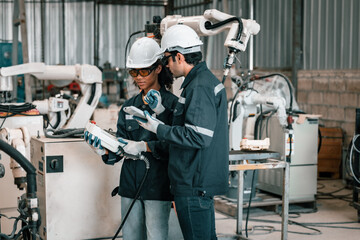 The robotic welding supervisor advice female worker to use a remote control panel display to...