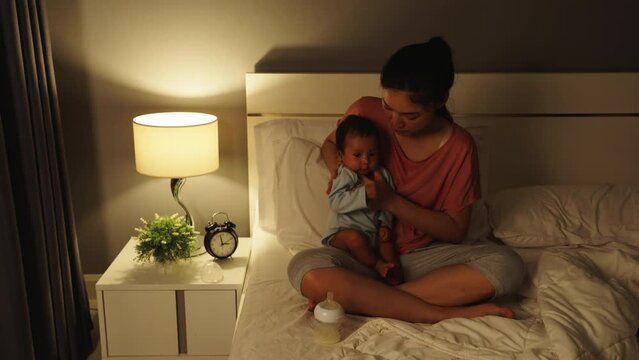 mother holding newborn baby burping after feeding milk on a bed at night