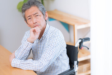 車椅子に乗った考えるシニア男性（介護・福祉）
