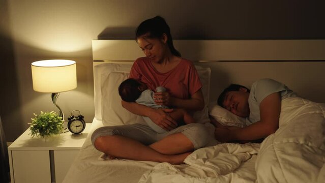 mother breastfeeding newborm baby while her husband sleeping on a bed at night