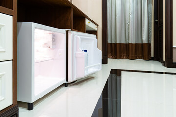 Refrigerator fridge mini size under the table counter with wooden desk beside it in hotel delux room.