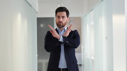 Handsome man crosses arms and says stop, don't do that in an office. Male appears serious and is likely giving warning or reprimand. Message of caution or to represent importance of following rules.