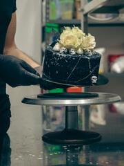 chef topping black airbrush painted frosted icing cake on top two real roses silver sprayed and...
