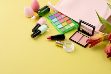 Obraz na płótnie Canvas Bright summer eyeshadow palette and makeup products in pink cosmetic bag on green background