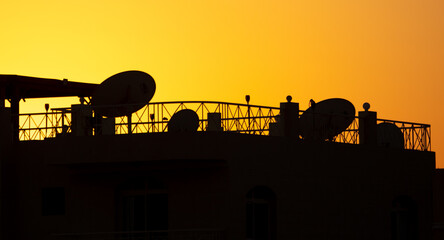 House roof silhouette with satellite dishes at sunset.