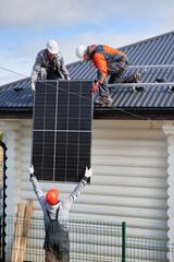 Professional technicians lifting up solar panel on a roof of house. Three workers in halmets and...