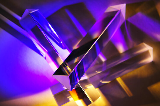 Closeup of group of reflective clear triangular prisms dispersing and spreading beam of light in to spectrum. Refracted magenta light with refraction on shiny surface. 