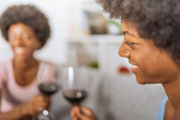 Black sisters with afro hairstyle, making a toast with a glass of red wine