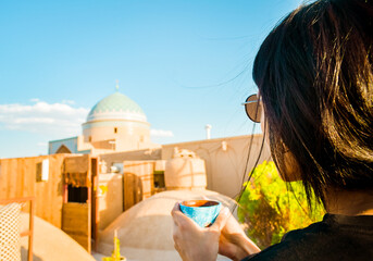 Yazd, Iran - 19th june, 2022: female caucasian tourist drink persian coffee in traditional rooftop cafe relax enjoy panoramic views of old town