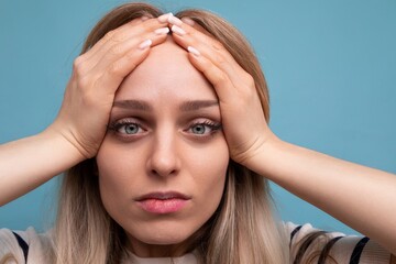 Fototapeta premium close-up of an upset girl in casual clothes holding her head on a blue isolated background
