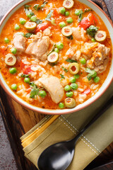 Asopao de pollo traditional Puerto Rican stew is rich with chicken thighs and green olives, adobo seasoning, garlic, cilantro, onions, and rice closeup on the bowl on the table. Vertical top view
