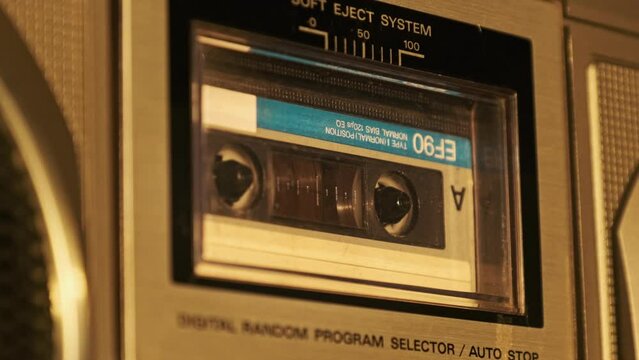The cassette is played in the tape recorder. Close-up. Audio cassette in deck playing and rotates. Vintage sound recording in old retro recorder. Call recording. Audiocassette playback. Macro