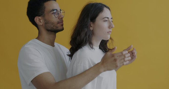 African American man covering woman's eyes then taking hands away while lady smiling enjoying surprise. People standing against yellow color background.