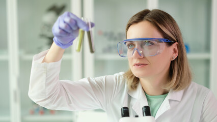 Woman chemist in protective glasses holding test tubes with liquid in hands in laboratory
