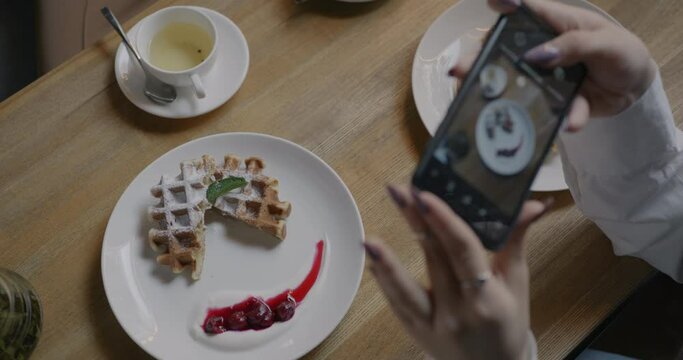 Close-up of female hands with smartphone taking picture of delicious coffee and dessert in cafe at table. Photo and food blogging concept.