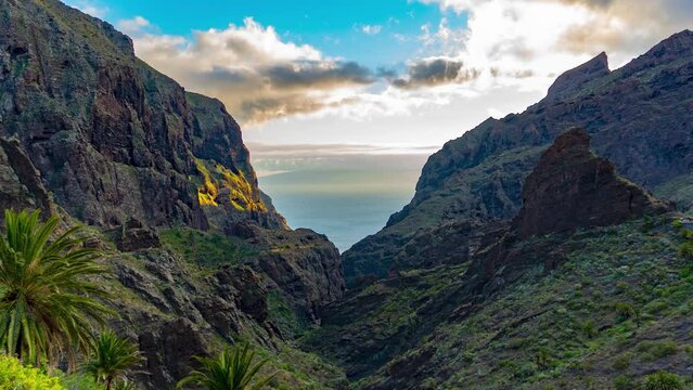 Sun Setting Over Maska Village With Palm Trees And Green Mountain Peaks, Orange Sun Rays, Mountain Valley, Ocean And Blue Sky In The Background, Time Lapse, Tenerife, Spain