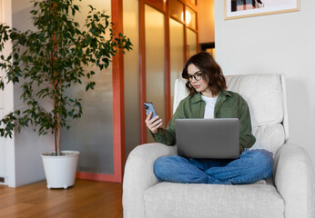 woman using laptop with phone at home