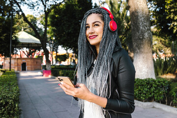 Young latin woman with braids hair listening to music with headphones and mobile phone on the street in Mexico, hispanic people