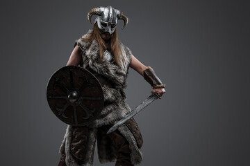 Studio shot of antique northern warrior with shield and sword against grey background.