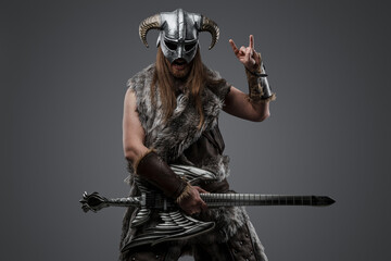 Portrait of viking in ecstasy dressed in fur and helmet playing electric guitar.