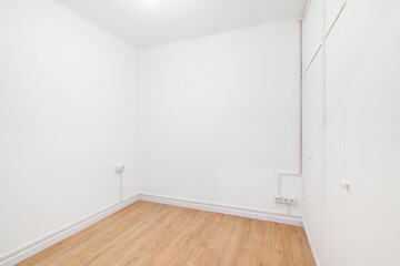 Fototapeta premium View of a small empty room with wooden laminate and electronic sockets in a new building. Concept of preparing a room for furnishing. Copyspace