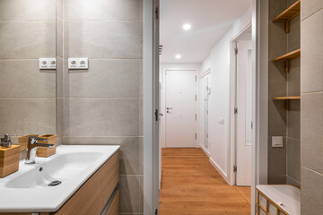 Fototapeta na wymiar Open bathroom with sink and gray tile, mirror, overlooking the hall with closet in a minimalist but stylish apartment. The concept of concise design. Hotel interior