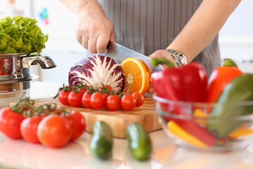 Cook cuts vegetables and fruits with knife on salad on board