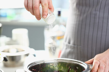 Cook pours salt into pan in kitchen