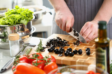 Male cook cuts black olives in kitchen