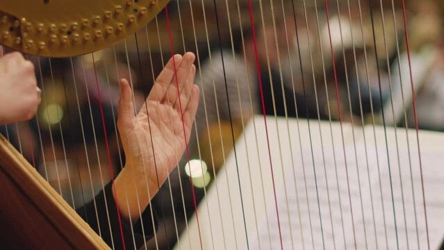 A slow motion video of a musician playing the harp by plucking only on one string during a classical symphony orchestra rehearsal