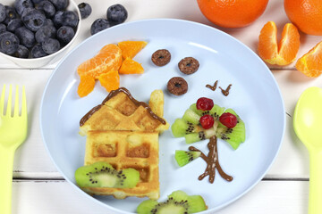 Children's breakfast: waffles and fruits on a blue plate. A creative idea for a fun kids dessert or breakfast