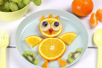 Fun food for kids. Cute appetizing fresh fruit chicken - orange, banana, blueberry - for a healthy breakfast with milk and biscuits