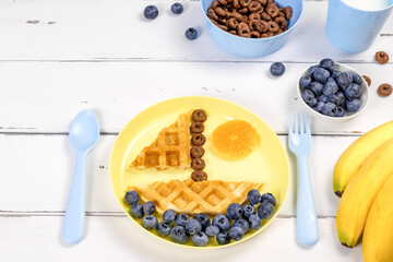 Boat of waffles with blueberries on a white wooden background. Funny food idea for kids.