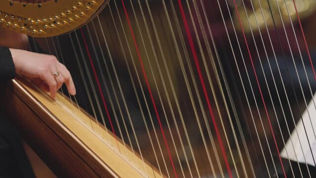A slow motion video of a musician playing a glissando on a harp during a classical symphony orchestra concert