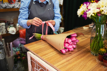 Naklejka na ściany i meble No face confident identical florist packs a bouquet of tulips in kraft makes a bow in a flower shop. Concept: flower delivery, personality, mothers day, womens day, valentines day, birthday, gift