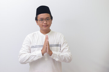 Portrait of young Asian muslim man showing apologize and welcome hand gesture. Isolated image on...