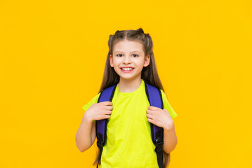 A schoolgirl with a backpack. A little girl with a satchel on her back. Teaching children. Supplementary education of the child. Educational, preparatory courses for school. Yellow isolated background